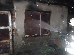 tűzoltó vízsugárral oltja a házat