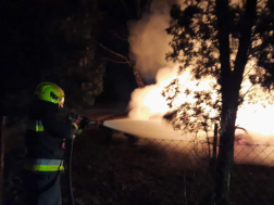 tűzoltó vízsugárral oltja az égő lakókocsit